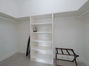 Empty walk-in closet with white shelves, an iron and ironing board on the left, and a luggage rack on the right.