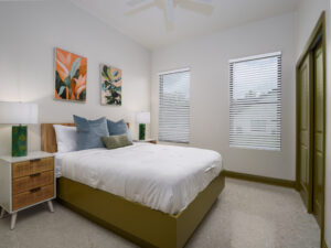 Modern bedroom with a double bed, two nightstands with lamps, abstract wall art, and two windows with blinds letting in natural light.