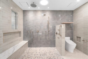 Modern accessible bathroom with a walk-in shower, grab bars, built-in bench, wall-mounted toilet, and grey tile walls.