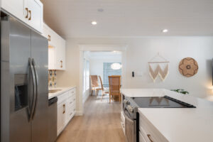 Modern kitchen with stainless steel fridge, white cabinets, and a view into a dining area with two wooden chairs and a round pendant light.