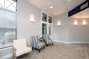 Modern waiting area with two striped chairs, one white armchair, a small table with a plant, a large rug, and neutral wall colors.