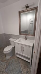 Modern bathroom with patterned tile floor, white toilet, and white vanity with sink, large mirror, and a wall-mounted light fixture above the mirror.