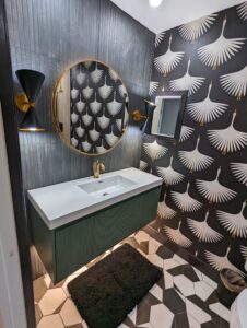 Modern bathroom with a round mirror, geometric floor tiles, crane-patterned wallpaper, black sconces, a green vanity, and a black rug.