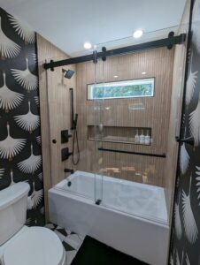 Modern bathroom with black and white crane wallpaper, a tub with glass shower doors, matte black fixtures, and a small horizontal window above the shower.
