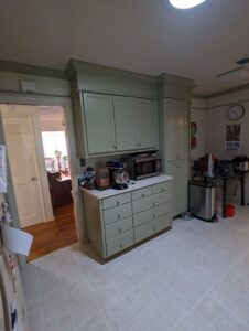 A kitchen with green cabinets, countertop appliances including a mixer and microwave, and a trash can near the wall.