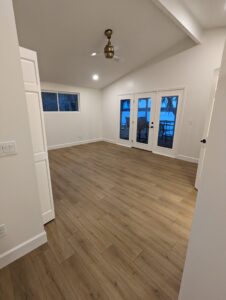 Empty room with light wood flooring, white walls, a ceiling fan, a side window, and glass double doors leading to an outdoor patio area.