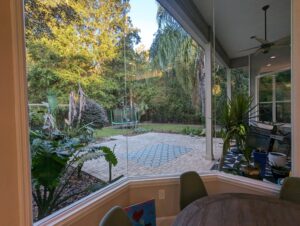 View from a window showing a patio with pavers, outdoor furniture, trampoline, plants, and a wooded backyard.